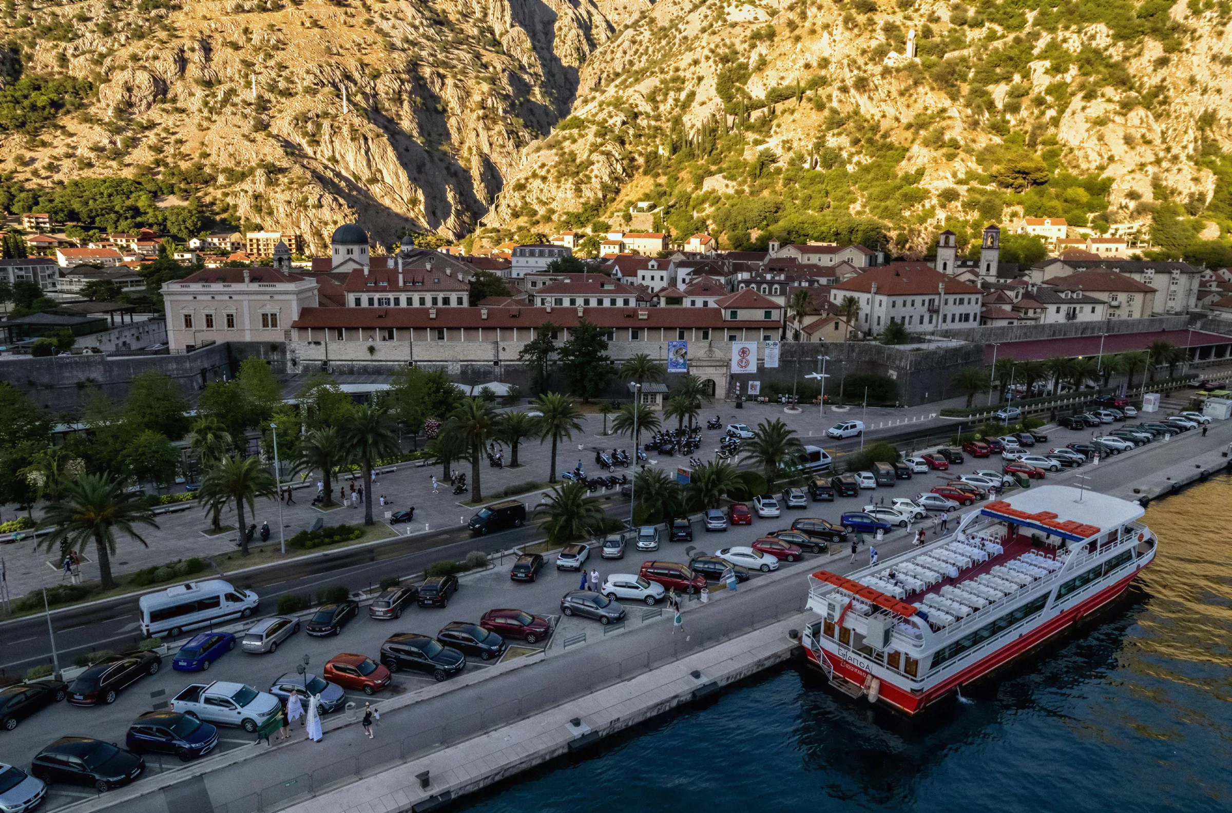 Katica moored on the Kotor waterfront below the old town walls, with the mountain rising behind