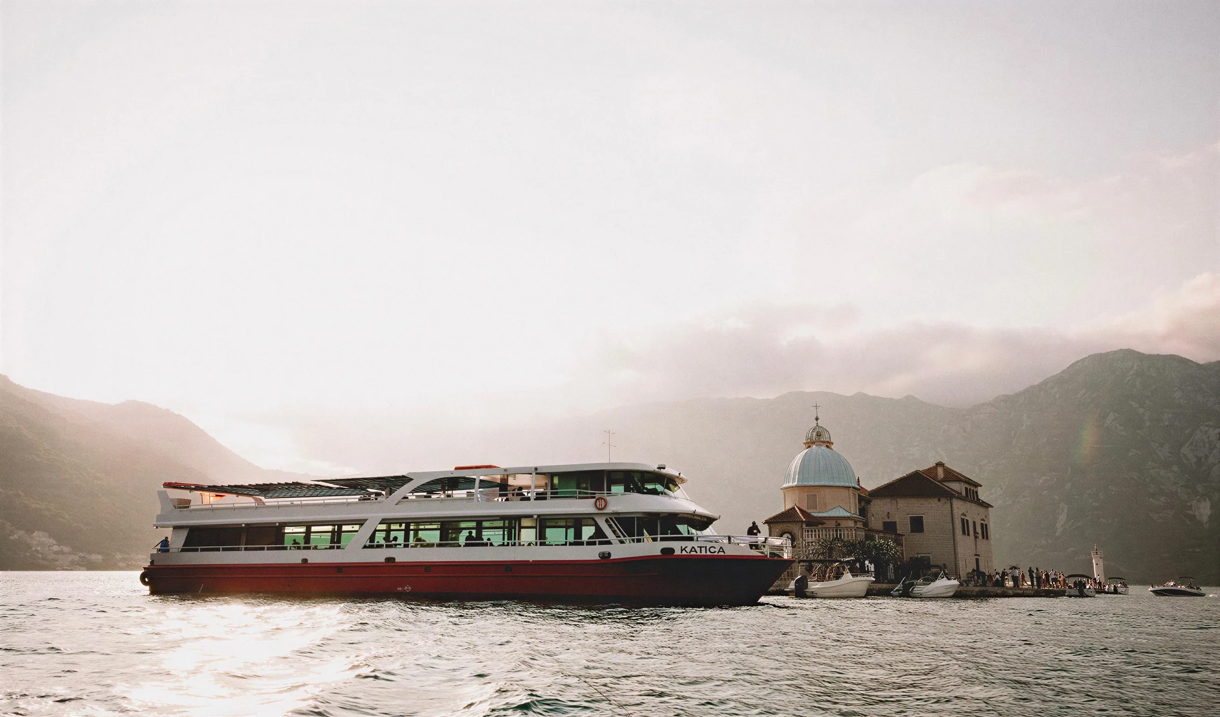 The Katica excursion boat alongside Our Lady of the Rocks island off Perast in the Bay of Kotor, in evening light