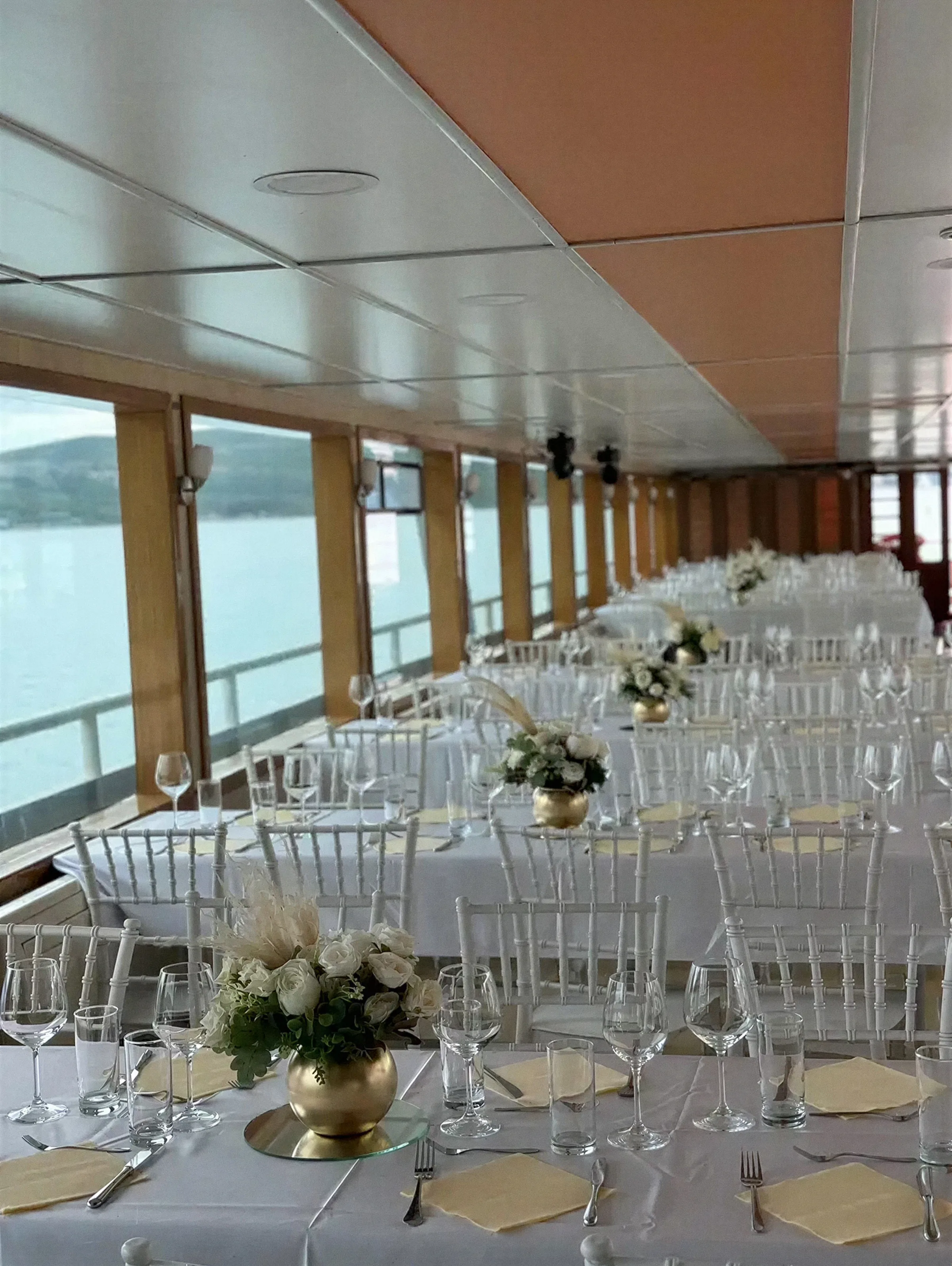 Long tables laid for dinner in the saloon of Katica during a private boat charter, the Bay of Kotor through the windows